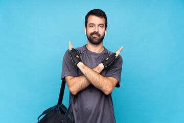Young sport man with beard over isolated blue background making NO gesture