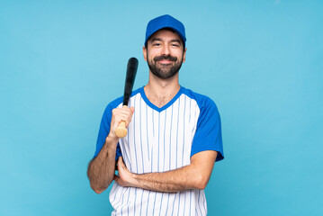 Young man playing baseball over isolated blue background keeping the arms crossed in frontal position