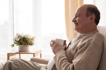 Joyful senior holding a white coffee cup dreaming about future plans