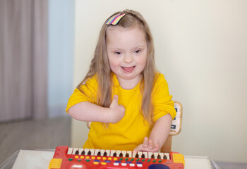 Down syndrome in a little girl, a child, a child playing a toy piano, early development of disabled...