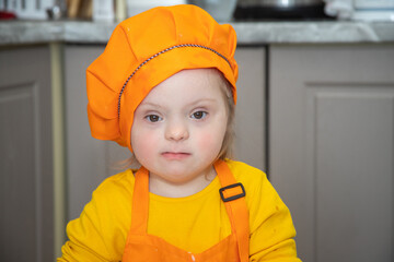 A little girl with Down syndrome prepares dough from flour, a disabled child dressed as a cook...