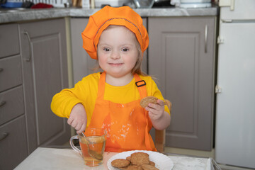 A beautiful girl with Down syndrome in an orange apron and a chef's hat, the girl is drinking tea...