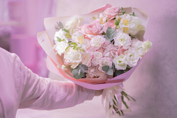 A man's hand is holding a lush beautiful bouquet of light pink, white cute delicate small roses of different sizes, flowers of green leaves. Romance.