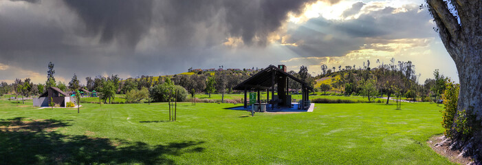 a stunning panoramic shot of a brown wooden pergola in the park surrounded by lush green grass and...