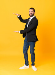 Fototapeta premium Full-length shot of business man over isolated yellow background holding copyspace to insert an ad
