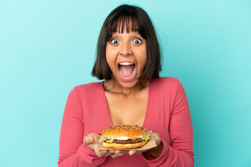 Young brunette woman holding a burger over isolated background