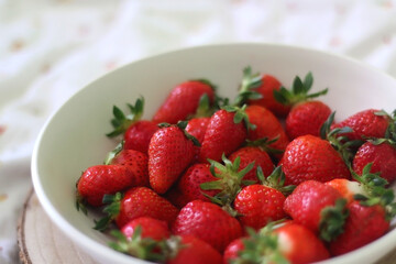 Bowl of fresh strawberries and wooden tray on a bed. Selective focus.