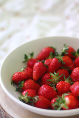 Bowl of fresh strawberries and wooden tray on a bed. Selective focus.
