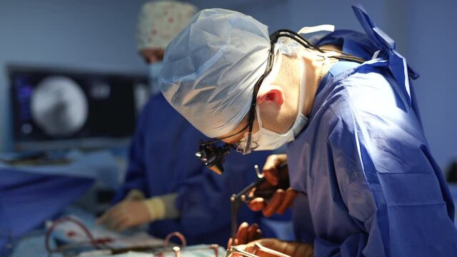 Doctor together with a nurse doing surgery. Professional surgeon in medical uniform and mask conducts an operation with surgical tools in the operating room.