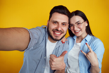 Couple takes selfie on cellular, makes like gestures over yellow background