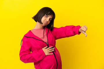 Young pregnant woman over isolated yellow background showing thumb down with negative expression