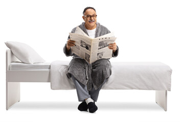 Mature man in  robe sitting on a bed and reading a newspaper