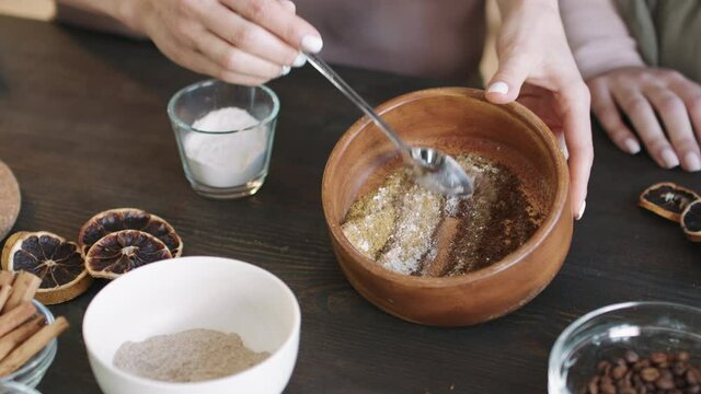 Midsection PAN top view shot of two unrecognizable women making face and body scrub at home, mixing bulk ingredients together in bowl