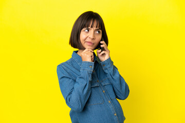 Pregnant woman using mobile phone isolated on yellow background and looking up