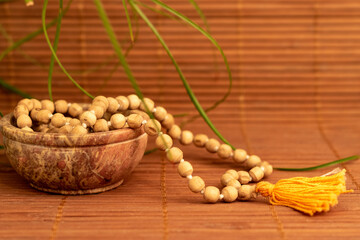 Wooden mala beads in ceramic bowl with green leaves against wooden background for copy space....
