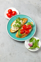Italian appetizer bruschetta with steamed tomatoes, basil and ricotta. On an aquamarine plate. Overhead, on a gray stone background, close-up