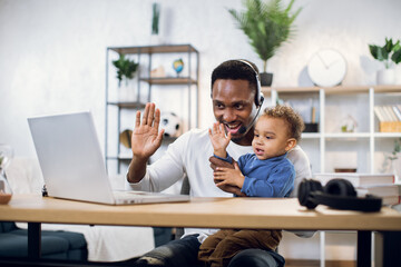 Afro american businessman with his little son on hands leading working meeting through video chat...