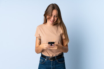Young Lithuanian woman isolated on blue background sending a message with the mobile