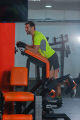 Side view of a middle-aged man with a yellow fluorescent shirt exercising on the machine for legs.