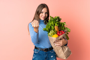 Young Lithuanian woman holding a grocery shopping bag inviting to come with hand. Happy that you came