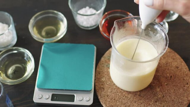 PAN top view shot of unrecognizable woman using hand mixer while mixing bee wax, shea butter and essential oils to make moisturizing body lotion