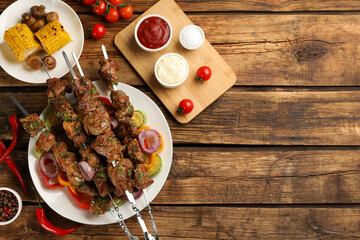 Metal skewers with delicious meat, sauces and vegetables served on wooden table, flat lay. Space for text
