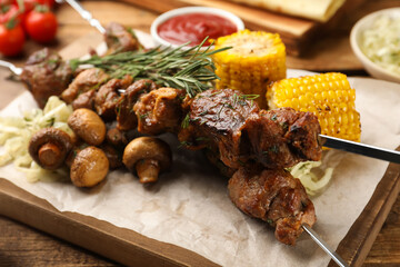 Metal skewers with delicious meat and vegetables served on wooden table, closeup