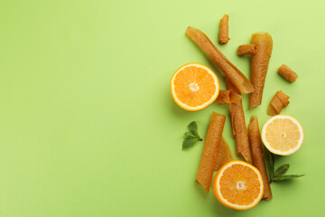 Delicious fruit leather rolls, mint, lemon and orange on green background, flat lay. Space for text