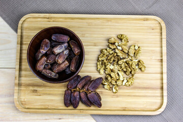 Fruit dates fruits. A bunch of walnut kernels. A sprig of date fruit with a wooden bowl of date fruit and a walnut kernel on a wooden tray.