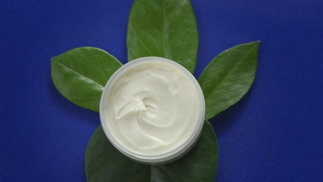 water flowing slow mo around Open jar of beauty cream on green leaves on blue background. Luxury hydration moisturizing natural herbal cosmetics to face and body. spa wellness center