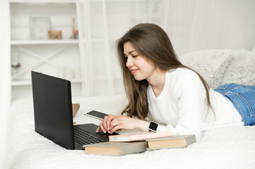 girl at home studying distance learning. a student sits at a laptop in her bed. remote work. online education of a young girl