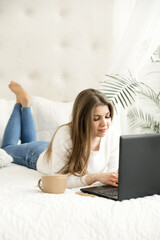 girl at home studying distance learning. a student sits at a laptop in her bed. remote work. online education of a young girl