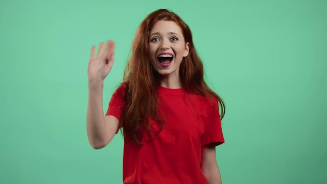 Friendly woman waving hand - hello, or goodbye, chao, adios. Parting, say bye to camera. Beautiful girl waving hand on green studio background