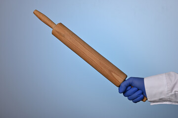 Doctor hand shows rolling pin. Medic hand holds wood cylinder for rolling dough. Rolling-pin in scientist hand to make handicraft bakery. Medic hand wearing a blue nitrile glove holds bakery utencil.