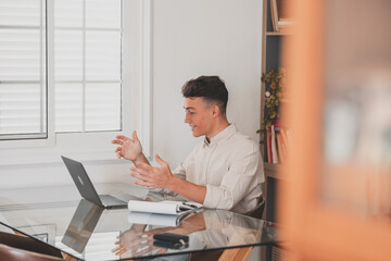 Happy young man teenager smiling and talking in video conference studying and learning online with school. Millennial doing homework at home calling .