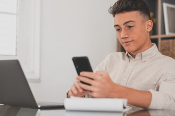 Happy young man teenager smiling and talking in video conference studying and learning online with school. Millennial doing homework at home calling from phone
