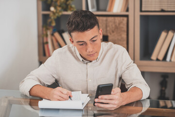 Happy young man teenager smiling and talking in video conference studying and learning online with school. Millennial doing homework at home calling from phone

