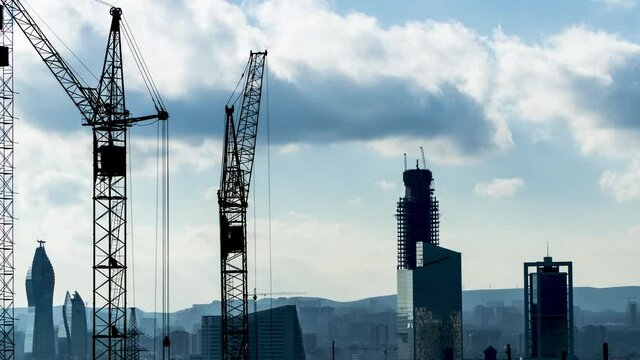 Self erecting tower cranes near high rise buildings under construction against beautiful cloudy sky. Industrial timelapse