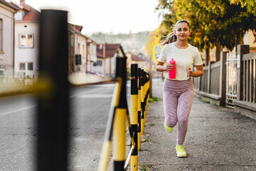 Front view full length of young caucasian woman running on the pavement in the city outdoor jogging in sunny day - sport fitness training and recreation concept real people copy space