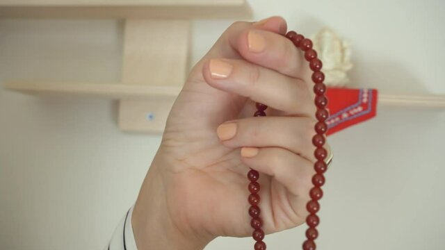 Woman's hand counts through red carnelian prayer beads with statuette of Hindu god, Ganesh (Ganesha), Lord of Letters and Learning, in background, 4K UHD