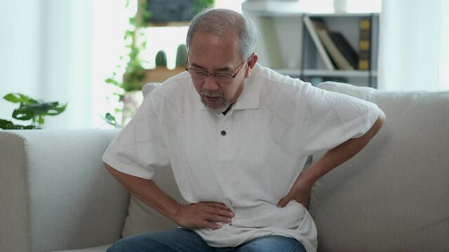 The Asian elderly man sit on sofa has a stomach ache. Caused by illness due to food poisoning