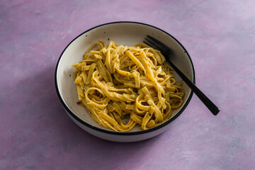 vegan lemon and herbs sauce fettuccini pasta on pink background, healthy plant-based food