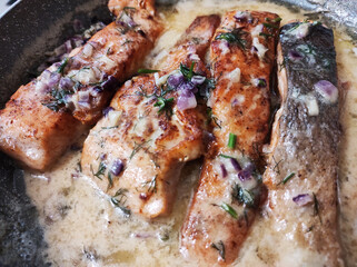 Fried salmon fillet in a pan with white sauce. 