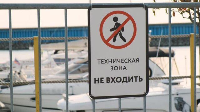 No trespassing sign in marina with boats in background. white prohibition sign with black outline of person in circle crossed out. Inscription in Russian language TECHNICAL ZONE DO NOT ENTER