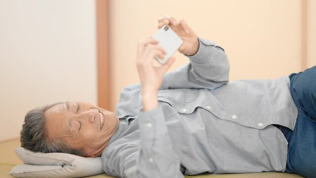 寝っ転がりながらスマートフォンを見るシニア男性