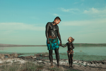 therapeutic mud for the body. mud baths on the lake. a man and a child are smeared with clay....