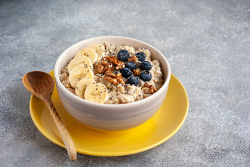 Healthy breakfast with oatmeal, banana, nuts and berries on yellow plate with wooden spoon.