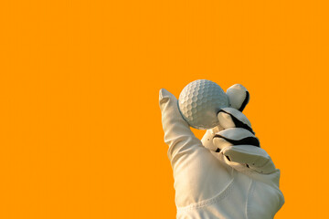 Golfer wearing golf glove showing golf ball on hand holding with orange color background.