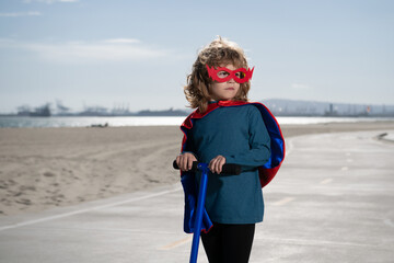Little kid boy plays superhero. Child on scooter in park. Kids learn to skate roller board. Little...