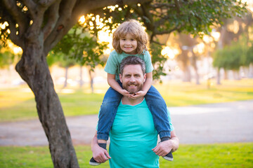 Happy father and son enjoying summer time on vacation in a sunny park. Dad carrying on shoulders...